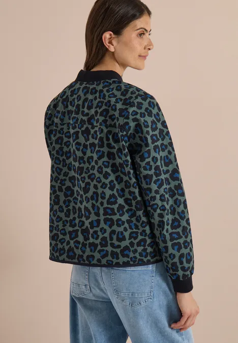 Frau trägt grüne, leo-bedruckte Jacke und blaue Jeans, seitlich von hinten fotografiert.