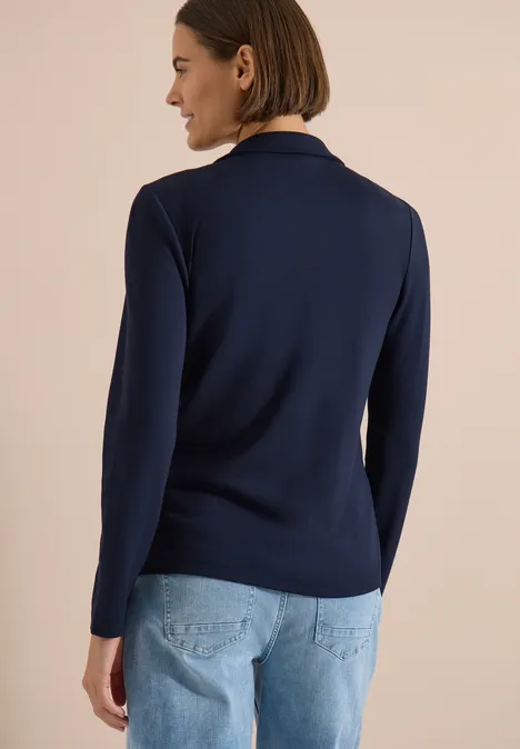 Person von hinten in dunkelblauem Pullover und hellblauer Jeans.