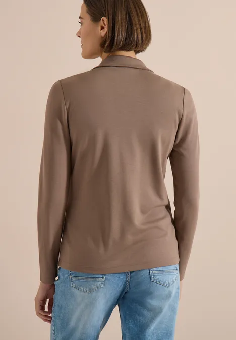 Frau von hinten mit kurzem Bob, trägt taupefarbenes Shirt und hellblaue Jeans.