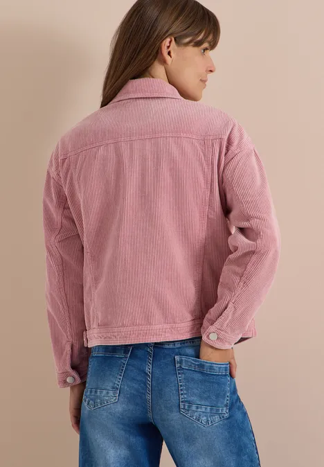 Une femme vue de dos portant une veste rose en velours côtelé et un jean bleu.