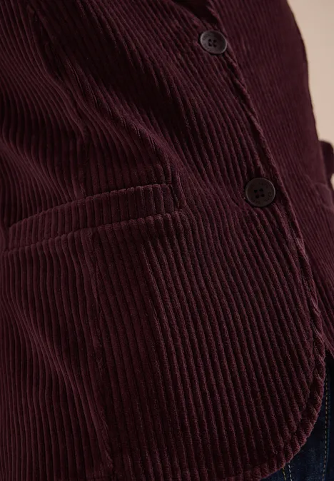 Nahaufnahme einer Person in einer burgunderroten Cord-Feinrippjacke mit Knöpfen und Tasche.