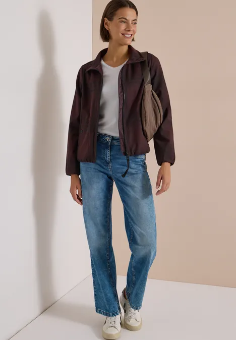 Frau im lässigen Outfit: Jeans, T-Shirt, Jacke, weiße Sneaker, lächelnd mit Tasche über der Schulter.