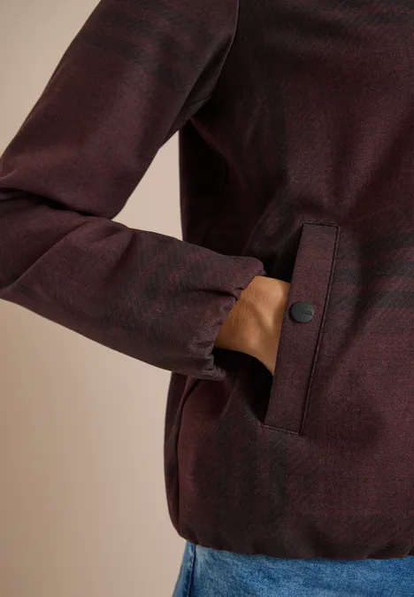 Person trägt bordeauxrote Jacke, Hand in seitlicher Tasche.