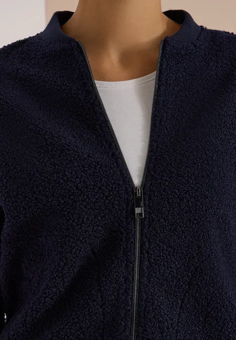 Dunkelblaue Teddy-Fleecejacke mit Reißverschluss über weißem Shirt.