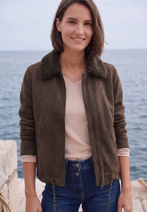 Velours Jacke mit Teddy-Kragen truffle brown Frau im braunen Blouson vor dem Meer, lächelt, trägt Jeans und beiges Shirt.