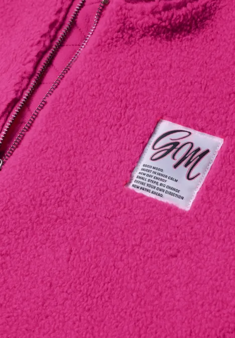 Close-up van een roze fleece trui met rits en witte GM-label.