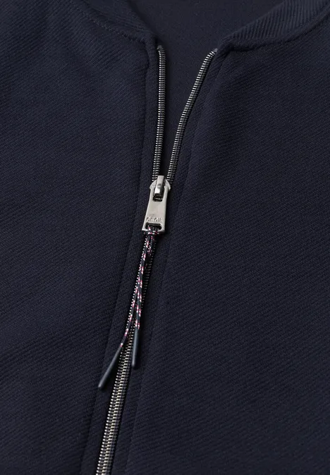 Close-up van een donkerblauwe, gestructureerde jas met een zilverkleurige rits en gevlochten koord