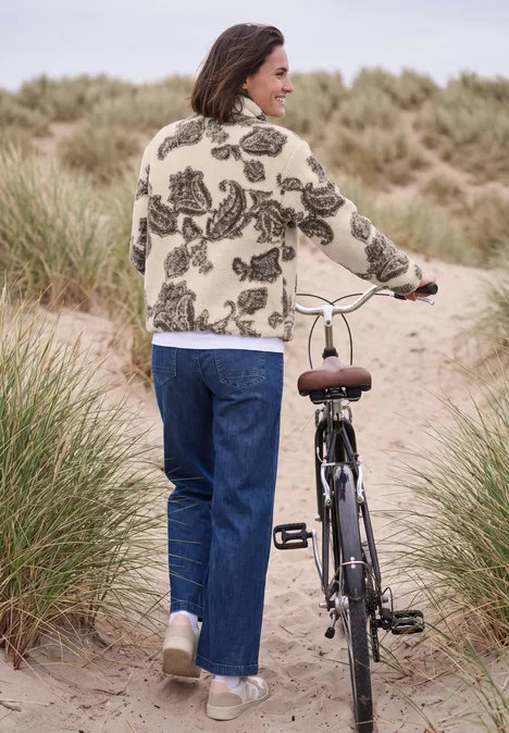 Eine Frau schiebt ihr Fahrrad auf einem Dünenweg, umgeben von Strandgras.