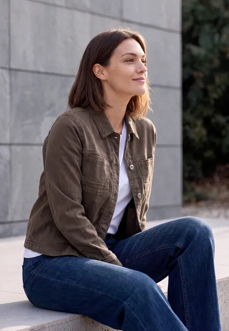 Denim Overshirt mit Brusttaschen truffle brown Eine junge Frau in Jeans und Jacke sitzt draußen und schaut nach oben.
