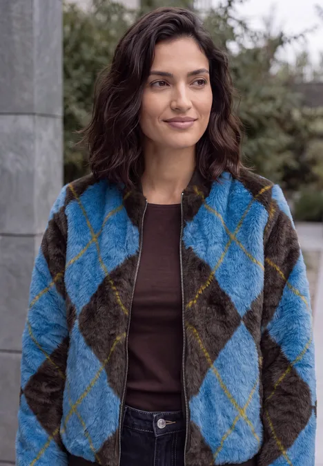 Fake Fur Blouson mit Argylemuster north blue Eine Frau trägt eine türkis-graue Rauten-Fleecejacke und ein braunes Shirt, steht draußen und lächelt leicht.