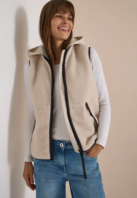 Teddy-Weste mit abnehmbarer Kapuze teddy vanilla white Frau trägt weiße Fleeceweste, weißes Langarmshirt und Jeans, lächelt locker.