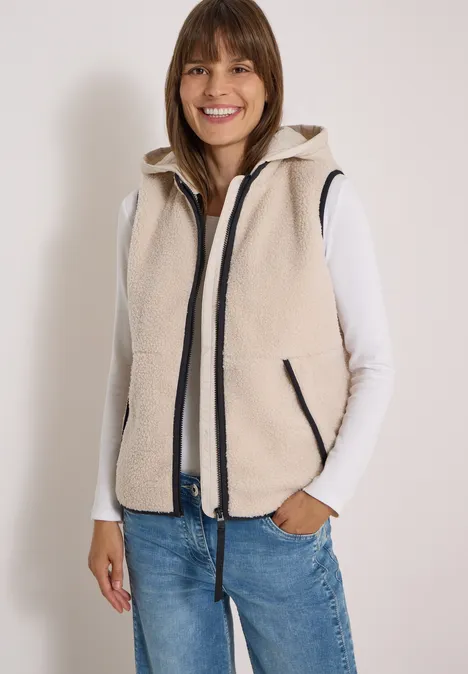 Teddy-Weste mit abnehmbarer Kapuze teddy vanilla white Frau trägt hellbeige Fleeceweste mit Reißverschluss über weißem Shirt und Jeans, lächelt.