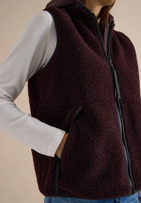 Teddy-Weste mit abnehmbarer Kapuze berry red Burgunderrote Teddy-Fleeceweste mit Reißverschluss, hoch schließendem Kragen und Seitentaschen über weißem Shirt.
