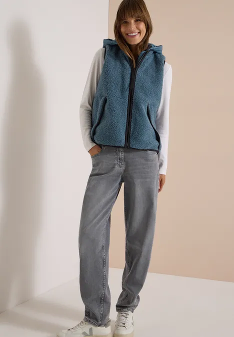 Teddy-Weste mit abnehmbarer Kapuze mountain air blue Eine Frau trägt einen grauen Hoodie, eine blaue Fleece-Weste und eine weite Jeans.