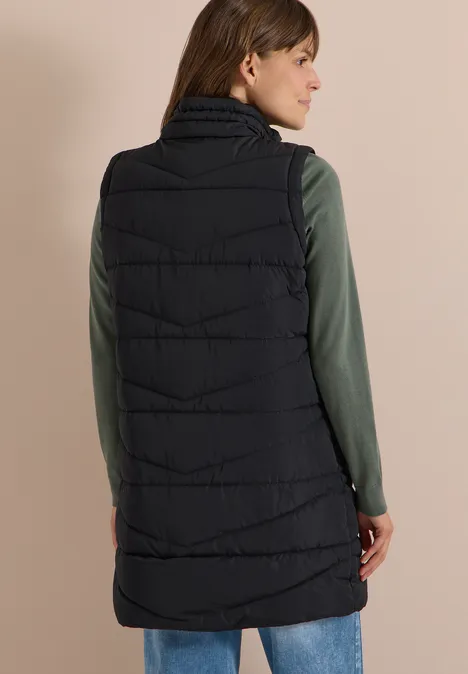 Femme vue de dos portant une longue doudoune noire sur un top manches longues vert.