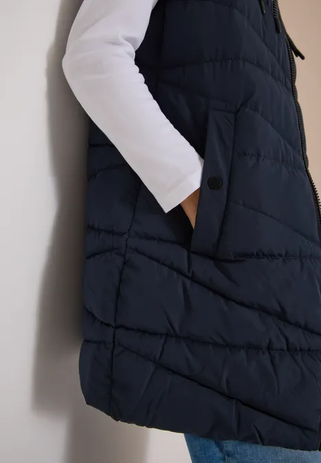 Vue latérale d'une veste matelassée bleu foncé sans manches avec poches, portée sur un t-shirt blanc et un jean.