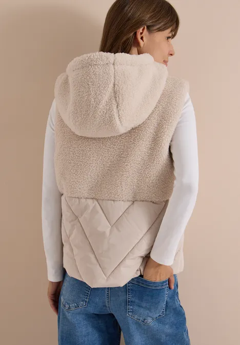 Vue de dos d’une femme en gilet sans manches en polaire beige à capuche et empiècement matelassé.