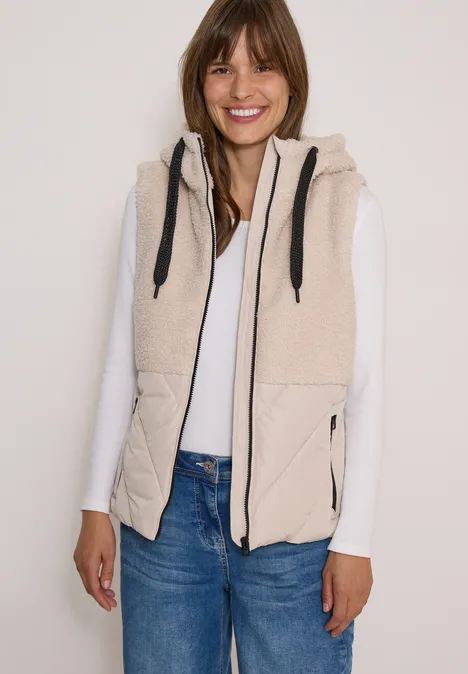 Femme porte un gilet beige à capuche sur un t-shirt blanc et un jean