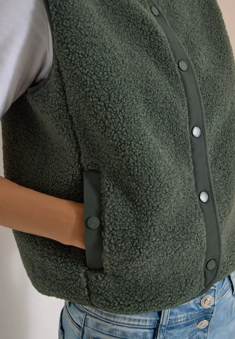 Smaragdgrüne Teddy-Fleece-Weste mit Druckknöpfen und Seitentaschen, darüber weißes Shirt und Jeans.