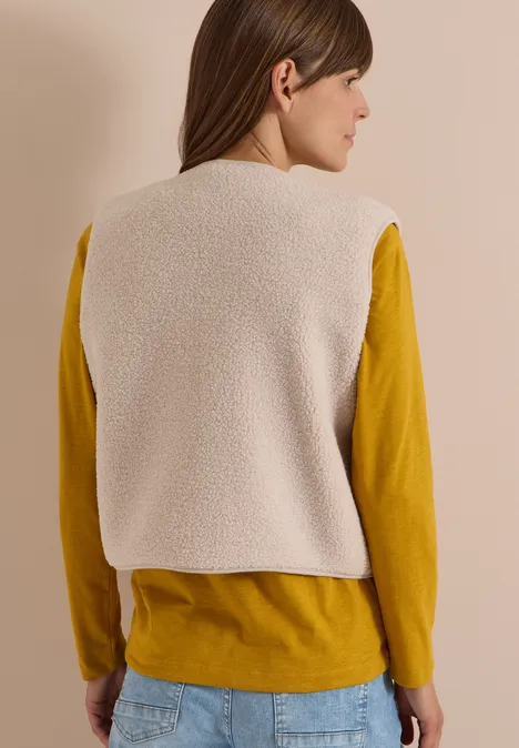 Teddy-Weste mit Softshelldetails teddy vanilla white Frau von hinten mit cremefarbener Teddyweste über senfgelbem Langarmshirt und Jeans.
