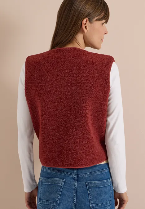 Teddy-Weste mit Softshelldetails russet red Person von hinten mit roter Fleece-Weste, weißem Langarmshirt und blauen Jeans.