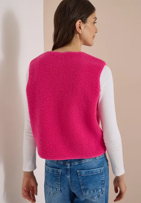 Eine Frau von hinten in einem pinken, flauschigen Strickweste, weißem Langarmshirt und blauen Jeans.