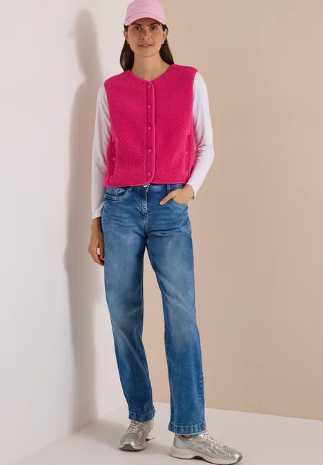 Frau trägt pink-weiße Strickjacke, blaue Jeans, graue Sneaker und pinke Baseballcap