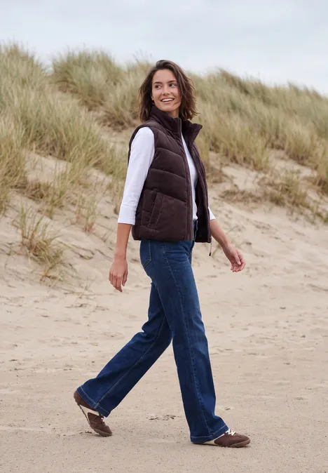 Vrouw in casual outfit wandelt over het zandstrand met duinen en helmgras op de achtergrond.