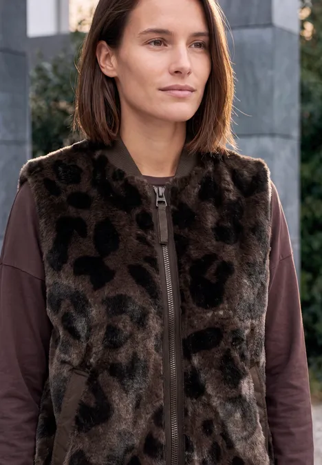 Teddyvest met gewatteerde details en patroon truffle brown Junge Frau in braunem Langarmshirt und Leopardenfellweste vor moderner Fassade, ruhiger Blick.