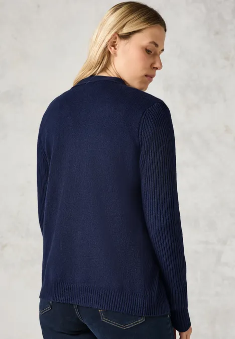 Frau mit langem Haar trägt dunkelblauen Strickpullover, steht mit dem Rücken zur Kamera.