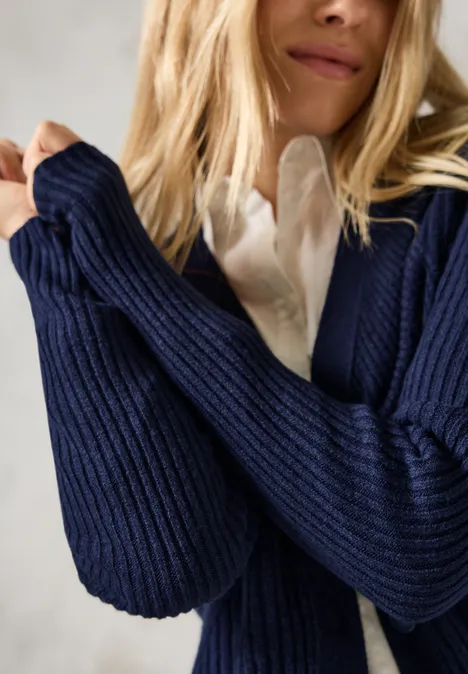 Frau in weißer Bluse und dunkelblauer Strickjacke, halb nah aufgenommen.