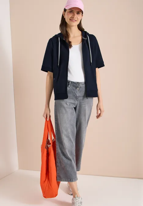 Kurzarm Sweatjacke mit Kapuze universal blue Frau mit weißem Top, dunkelblauer Kurzarmjacke, grauen Jeans und orangefarbener Tasche.