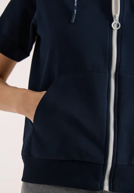 Kurzarm Sweatjacke mit Zipper universal blue Eine Person trägt einen dunkelblauen Kapuzenpullover mit Reißverschluss und steckt die Hand in die Fronttasche.
