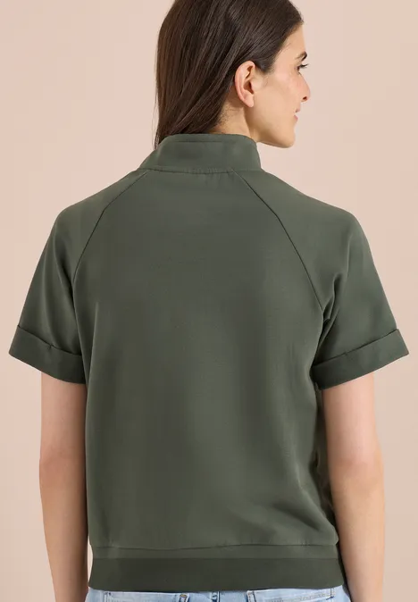 Kurzarm Sweatjacke mit Zipper khaki Frau von hinten in olivgrünem Kurzarm-Poloshirt, Haare halboffen, vor neutralem Hintergrund.