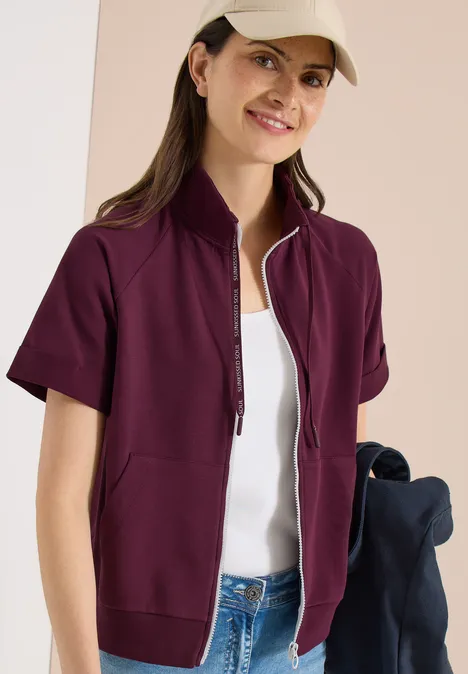 Kurzarm Sweatjacke mit Zipper sweet grape red Eine Frau trägt eine kurze, weinrote Jacke mit Reißverschluss über weißem Top und Jeans.