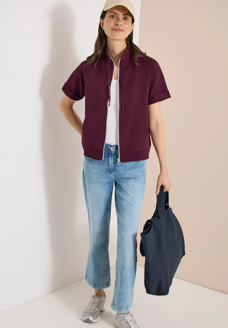 Kurzarm Sweatjacke mit Zipper sweet grape red Person mit lila Kurzarm-Jacke über weißem Shirt, blauen Jeans, grauen Sneakern, hält eine dunkelblaue Tasche.