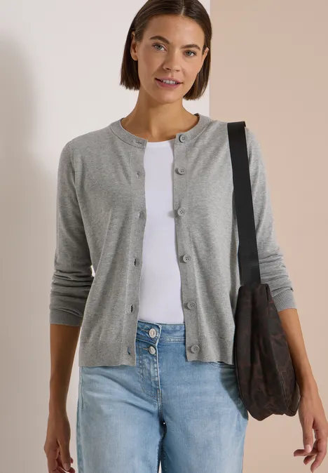 Frau in grauem Cardigan, weißem Shirt und Jeans, mit Tasche über der Schulter.