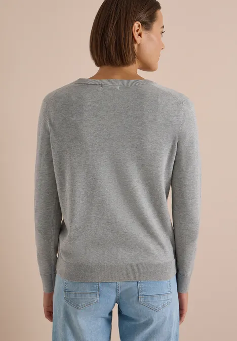 Rückenansicht einer Person mit grauem Pullover und blauer Jeans vor hellem Hintergrund.