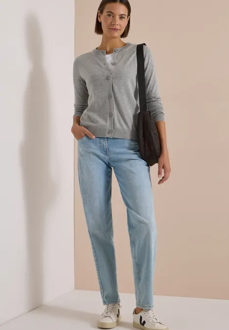 Eine Frau in grauem Cardigan und blauer Jeans trägt eine Tasche und lässige Espadrilles.