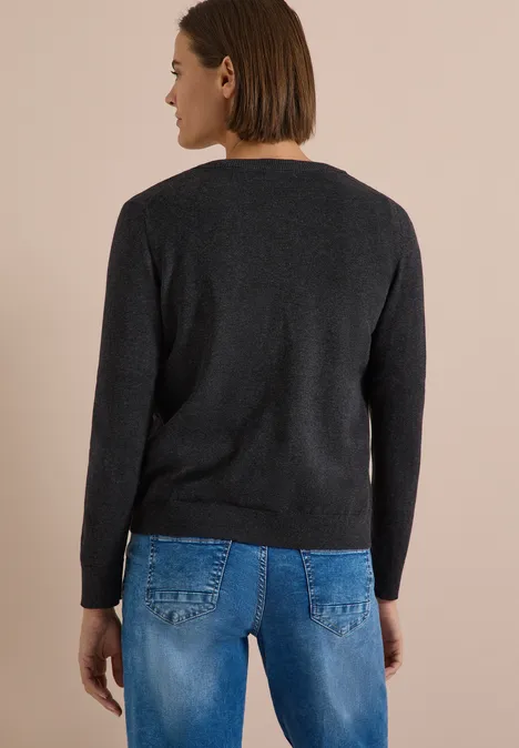 Rückansicht einer Frau in schwarzem Pullover und blauen Jeans vor hellem Hintergrund.
