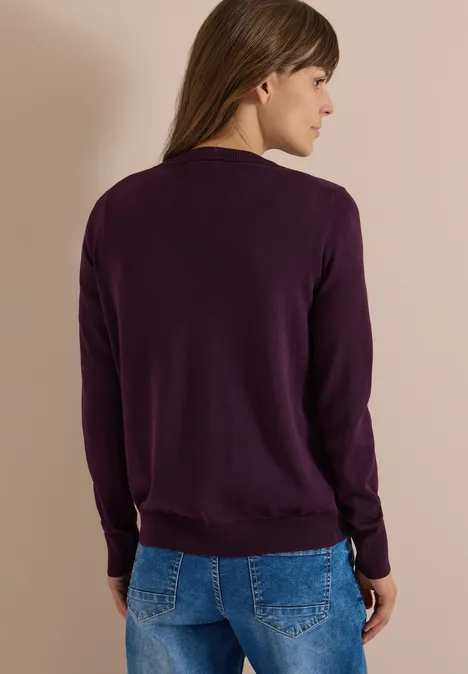 Cardigan mit Rundhals und Knopfleiste eggplant red Frau von hinten in lila Pullover und Jeans vor beigem Hintergrund.