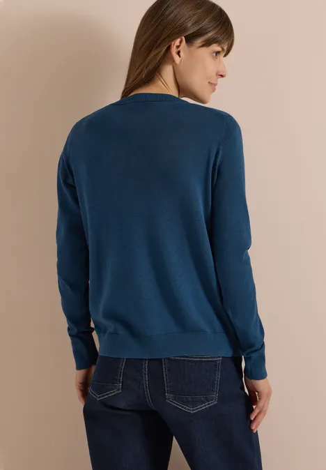 Cardigan mit Rundhals und Knopfleiste moonlight blue Eine Frau steht in dunkelblauem Pullover mit langen Ärmeln und Jeans, Aufnahme von hinten vor beigem Hintergrund.