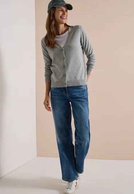 Cardigan mit V-Neck und Knopfleiste mineral grey melange Eine Frau in grauer Strickjacke, Jeans und Baseballkappe, lässig stehend mit Sneakern vor neutralem Hintergrund.