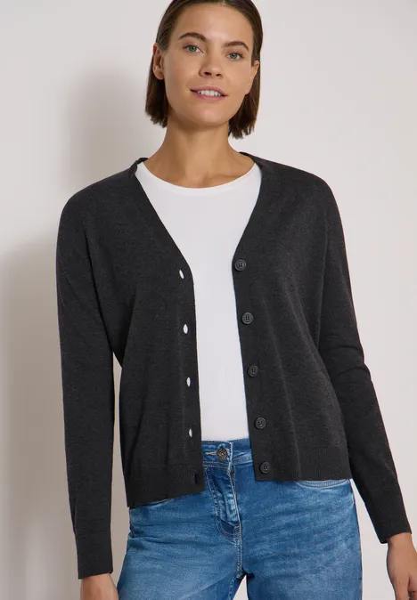 Frau mit anthrazitfarbenem Cardigan, weißem Shirt und Jeans.
