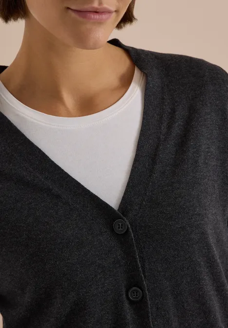 Nahe Ausschnitt: Weißes Rundhalsshirt unter dunkelgrauer, geknopfter Strickjacke.