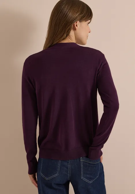 Frau von hinten in dunkelviolettem Langarm-Pullover und Jeans vor neutralem Hintergrund.