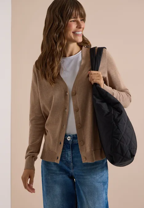 Vest met V-hals en knoopsluiting creamy mocha melange Frau mit beiger Strickjacke, weißem Top, Jeans und schwarzer Umhängetasche lächelt und schaut zur Seite.