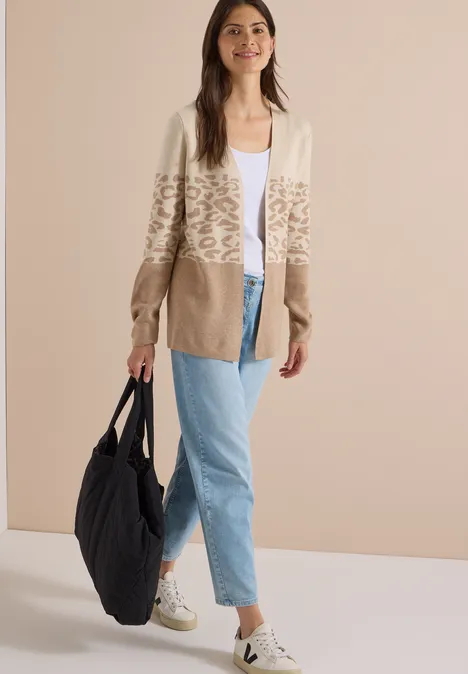 Offener Cardigan mit Jacquard-Muster creamy mocha melange Modell in beiger, Leo-Print-Strickjacke, weißem Top, hellblauen Jeans, weißen Sneakern und großer schwarzer Schultertasche.