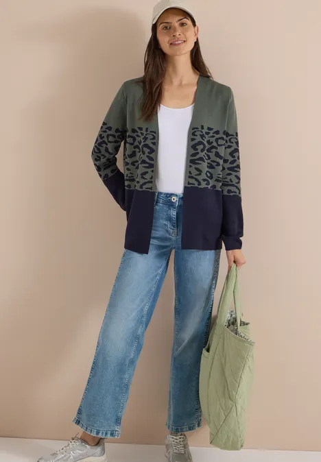 Offener Cardigan mit Jacquard-Muster dried olive green Frau im Cardigan mit grün-schwarzem Muster, weißem Shirt, lockeren Jeans und grüner Tasche.