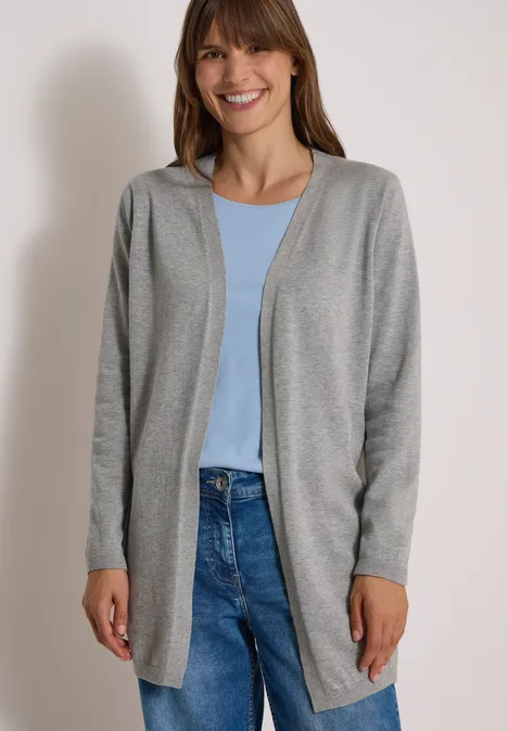 Lang, openvallend vest mineral grey melange Frau im grauen Cardigan, blauem Shirt und Jeans lächelt vor neutralem Hintergrund.
